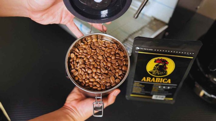 Tay đổ hạt Arabica rang mộc vào hũ bảo quản kín khí.