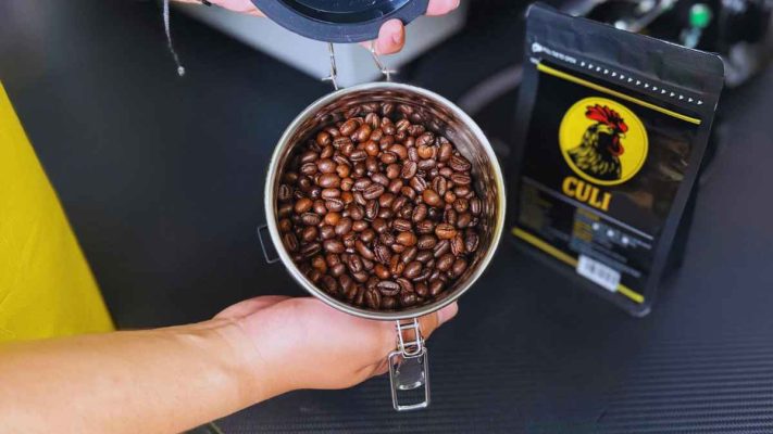 Tay đổ hạt cà phê Culi rang bơ vào hũ kín khí để bảo quản.