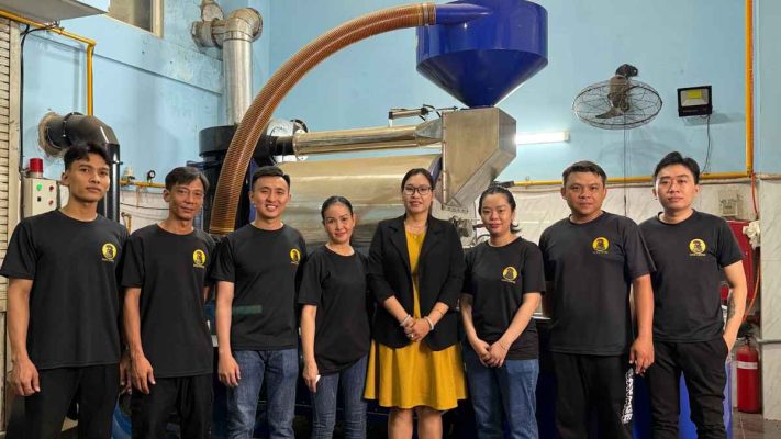 Nhân sự Lyon Coffee đứng cạnh máy công nghiệp rang xay cà phê Robusta rang mộc
