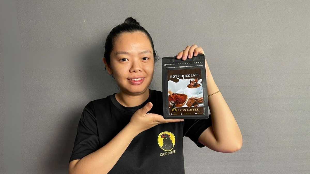 Túi Bột Chocolate Nguyên Chất Lyon Coffee 500g đặt cạnh tách socola nóng và thanh chocolate đen