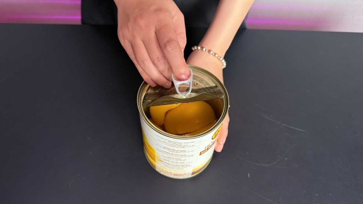 Hộp thiếc Đào Boddob Yot Doi nắp bật đặt cạnh muỗng gỗ và ly đá lạnh