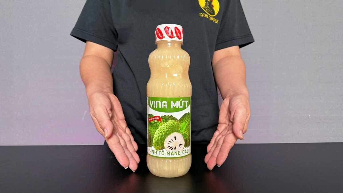 Chai Sinh Tố Vina Mãng Cầu 1L đặt cạnh ly sinh tố mãng cầu đá xay màu trắng ngà