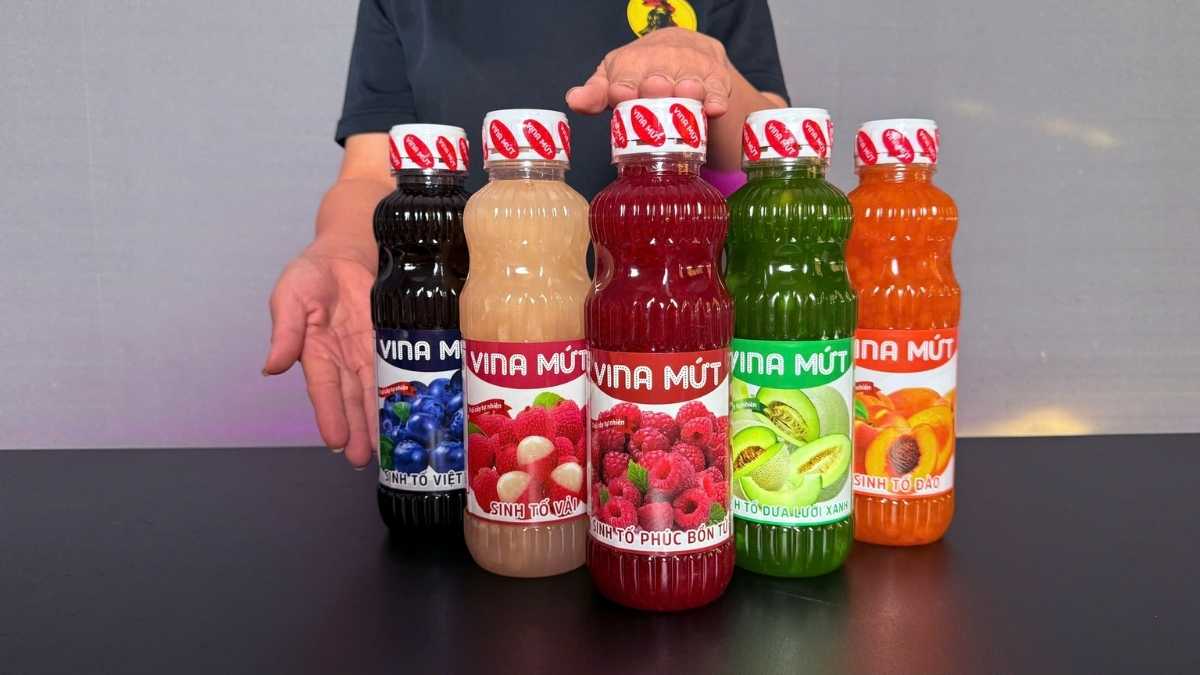 Logo Vina Mứt San Hô Xanh cạnh chai Sinh Tố Phúc Bồn Tử trên nền trắng