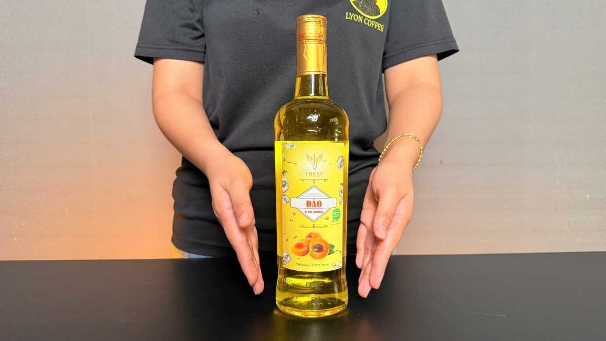 Barista pha trà trái cây với Siro Frusy Đào chai 750 ml màu vàng cam tươi.