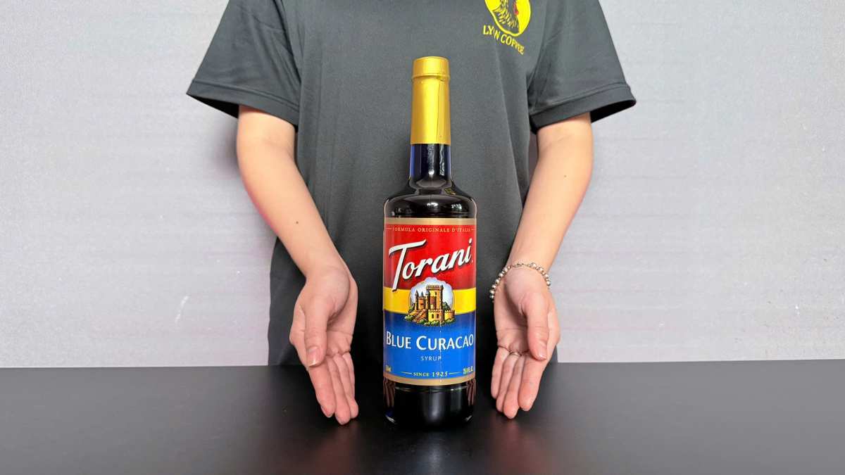 Ly soda Torani Blue Curacao đặt trên bàn gỗ cạnh lát cam và đá lạnh