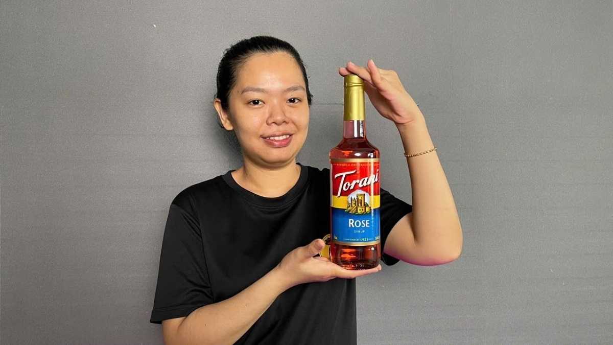 Chai Siro Torani Hoa Hồng 750ml đặt cạnh ly trà hoa hồng hồng phấn trong quán cà phê sáng
