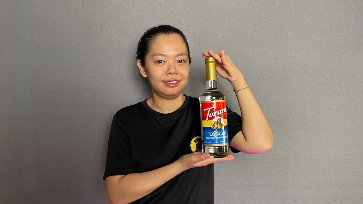 Chai Siro Torani Nhãn 750ml đặt cạnh ly trà nhãn lạnh có lát nhãn tươi trang trí