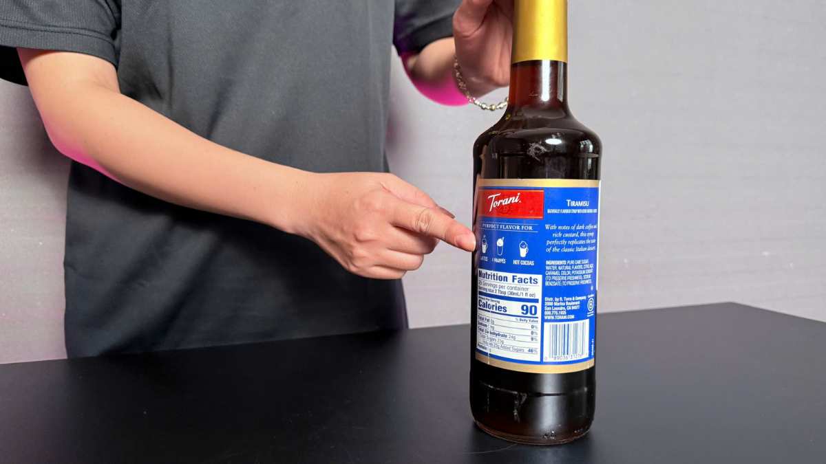 Tay khách cầm ly cà phê tiramisu nhìn qua lớp bọt sữa mịn và mùi thơm lan tỏa