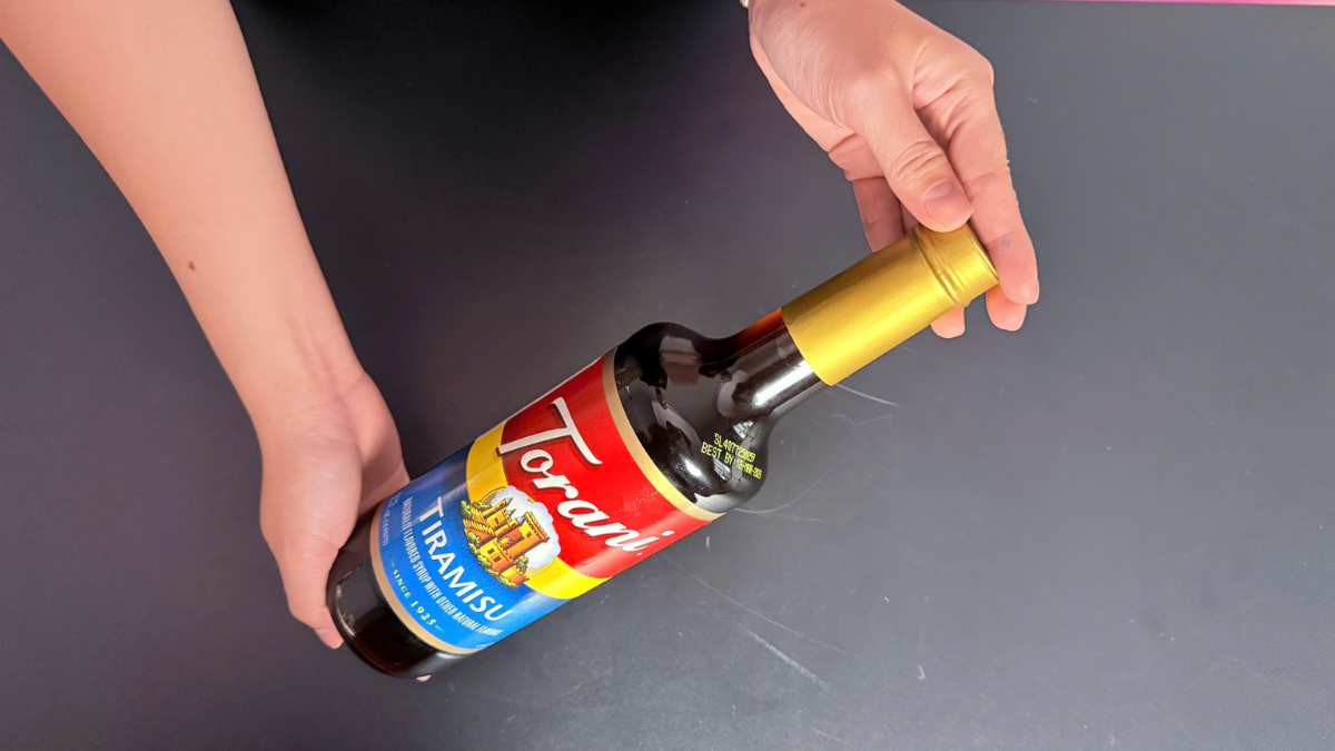 Logo Torani USA in nổi trên chai thủy tinh nâu nền quầy bar sáng vàng