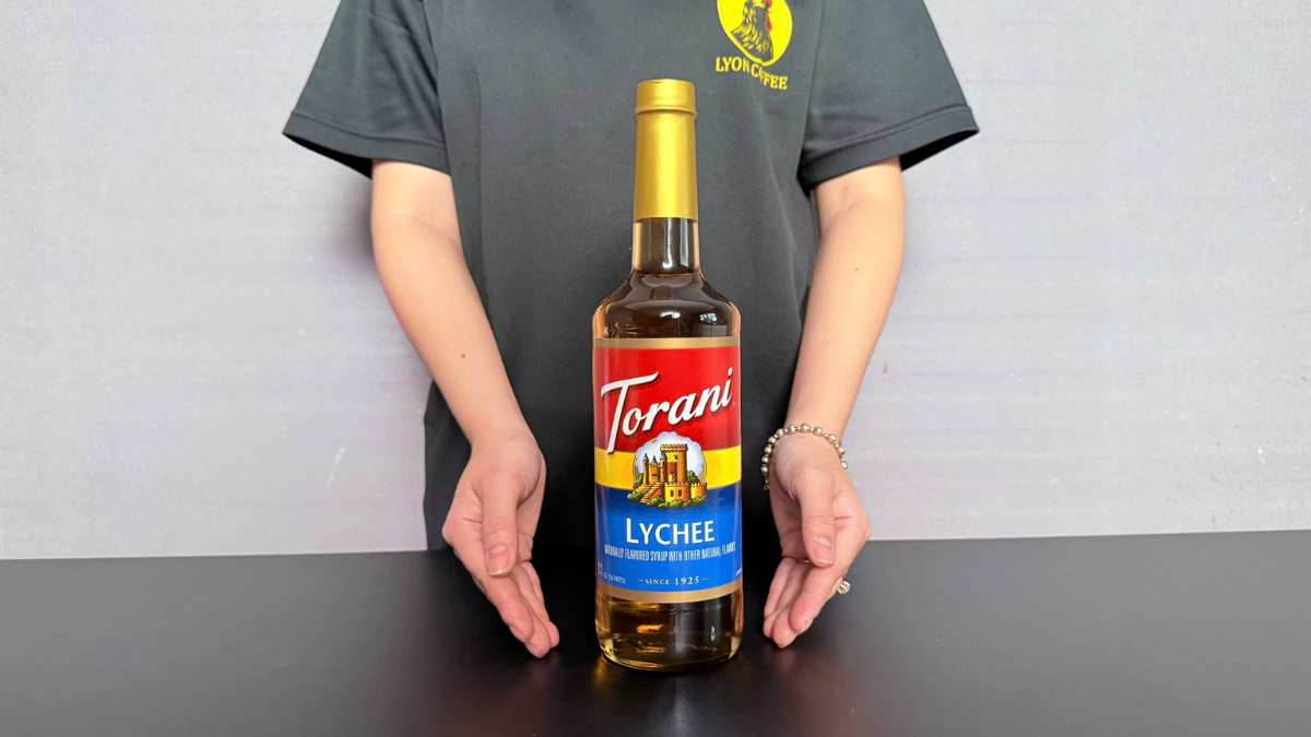 Ly trà vải Torani trên nền gỗ sáng với lát vải tươi và lá bạc hà