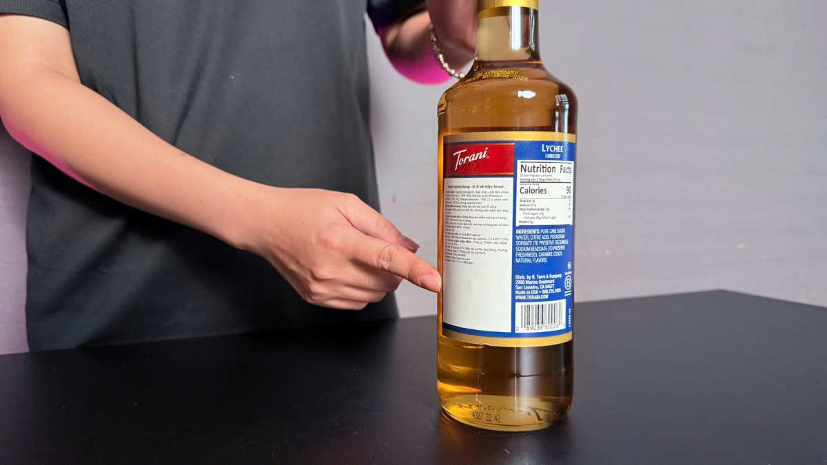 Giọt siro Torani Vải trong suốt rơi xuống ly soda, ánh sáng hồng phản chiếu