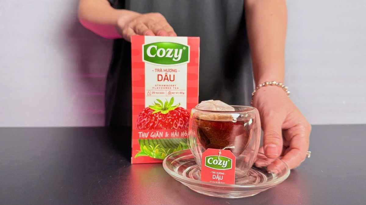 Tách trà Cozy Hương Dâu nóng bốc khói, đặt cạnh lát dâu tươi và muỗng gỗ